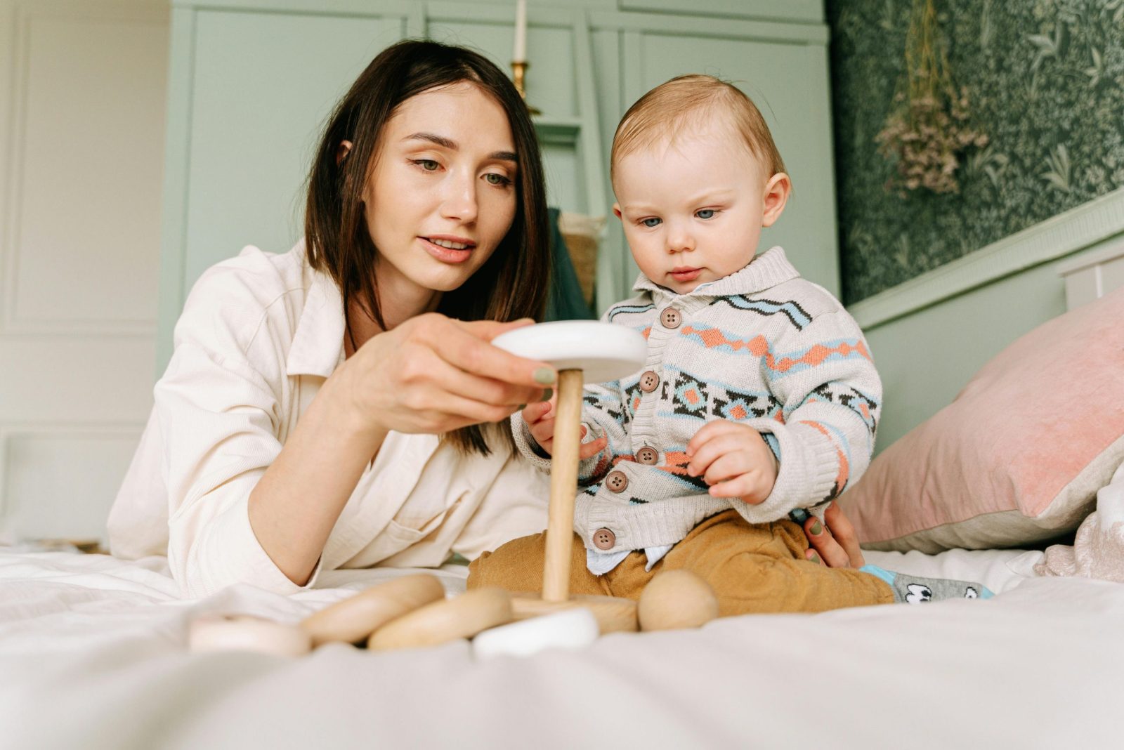 A mother and baby play together on a bed with wooden toys, fostering closeness and learning.